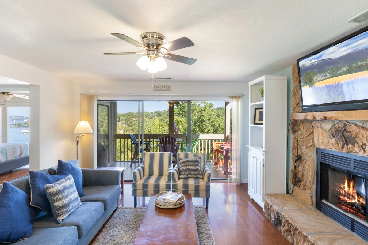 A spacious living room outfitted with a plush sofa, striped chairs, a fireplace, and large windows that offer expansive views of lush greenery. The atmosphere is warm and inviting, suggesting moments of relaxation, gathering, and enjoying the natural surroundings even from indoors.
