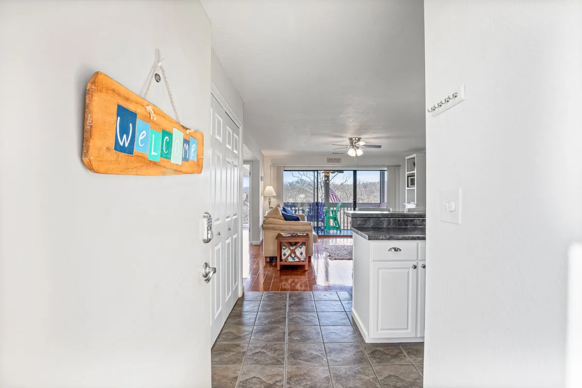 A warmly lit interior featuring a kitchen counter with a visible welcome sign and a glimpse into the adjacent living area. The open concept makes the space feel inviting, perfect for entertaining and family gatherings, with a hint of the outdoors visible through the windows.