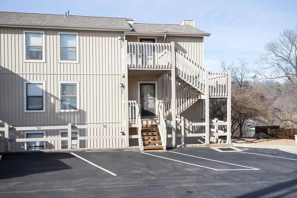An exterior shot showing the front of a condo building with a welcoming staircase, front door, and adjacent parking area. The communal vibe is enhanced by shared outdoor spaces, inviting arrivals and gatherings.