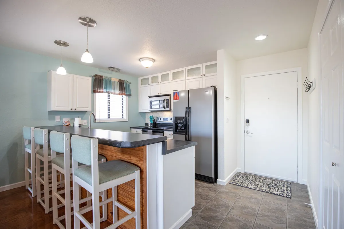 A spacious, inviting kitchen featuring a central island, modern refrigerator, ample countertop space, elegant light fixtures, and a window with curtains that brings in natural light. The layout encourages both cooking and conversation, making it ideal for preparing meals and gathering with family or friends.
