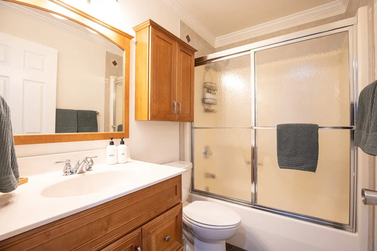 A modern, updated bathroom with a vanity and sink, a spacious shower area, wood cabinetry, and a large mirror. The space feels fresh and inviting, providing a sense of privacy and relaxation for morning and evening routines.