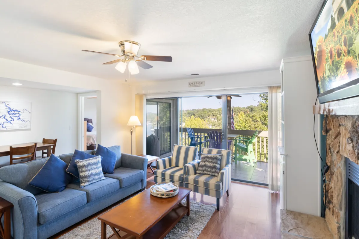 A spacious living area featuring a blue sofa, striped chairs, a wooden coffee table, and large windows that open up to a scenic view. The atmosphere is welcoming and ideal for group activities or simply soaking in the sunset.