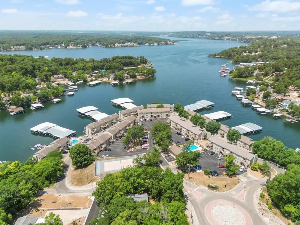 A wide view encompassing the lakefront, marina, pool, and pathways, this image blends aquatic amenities with serene natural beauty. People can be seen engaging in lake activities like boating and swimming, while landscaped paths encourage strolls and exploration.