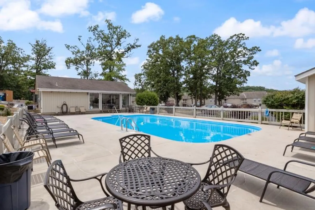 This exterior image features a sparkling swimming pool surrounded by ample outdoor seating and mature trees, offering a glimpse of how residents can gather, swim, and relax in a pleasant natural setting. The image evokes a resort-like atmosphere with opportunities for both recreation and peaceful leisure.