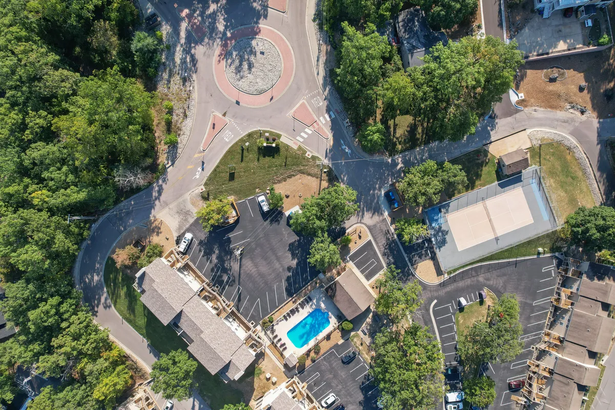 The scene shows a swimming pool adjacent to a basketball court, framed by trees and open communal spaces. The image captures the vibrant, communal side of the amenities, showing both water and court activities alongside spaces for gatherings and relaxation.