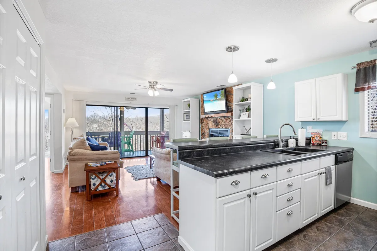 An inviting view of the open-plan kitchen and living area, featuring a kitchen island, comfortable seating, and sliding glass doors leading out to the balcony. The space is bright and airy, ideal for cooking, hosting, and relaxing, with seamless access to fresh air and outdoor dining.